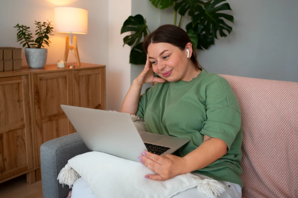 Woman with earbuds on a laptop video call from her couch at home